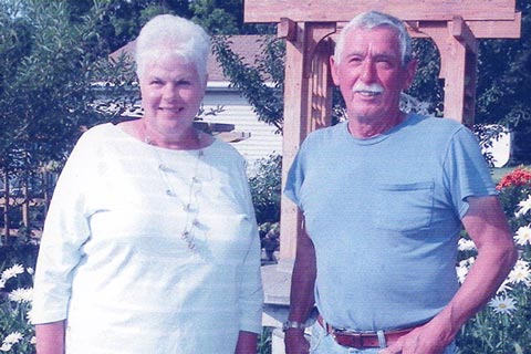 Dan and Lynn Adams standing in front of a flower garden with an arbor
