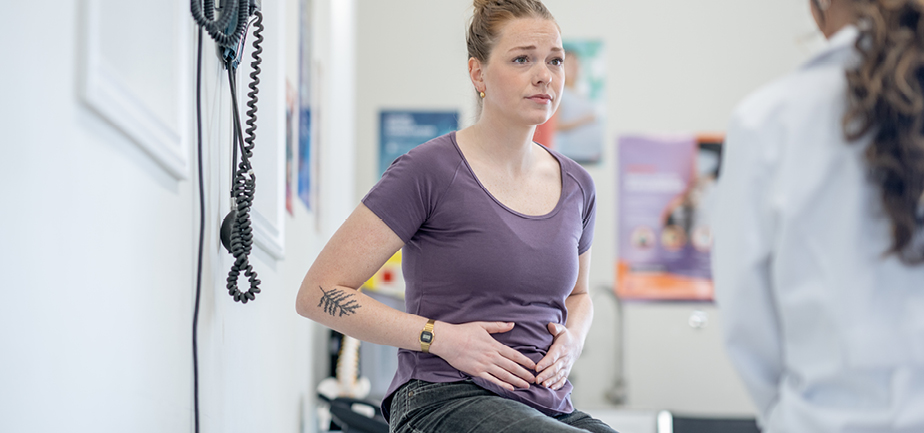 woman in doctors office holding stomach talking to doctor