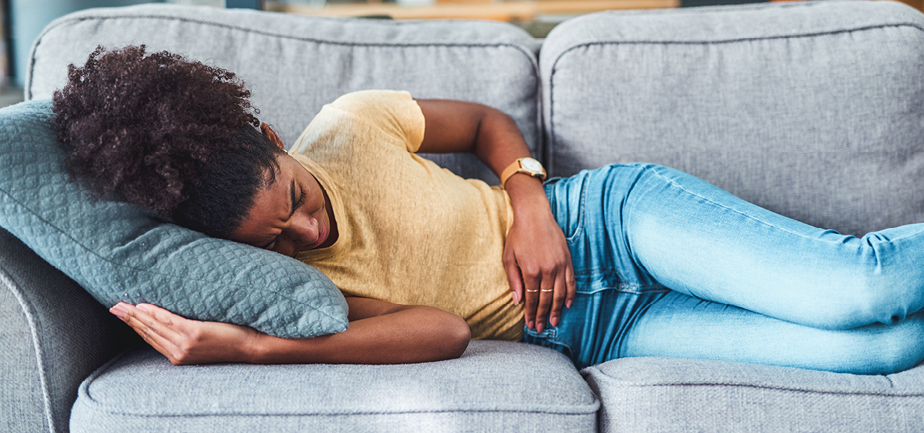 woman on couch holding stomach in pain