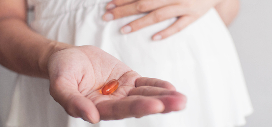 Midsection of a pregnant woman holding a yellow colored medicine gel capsule.