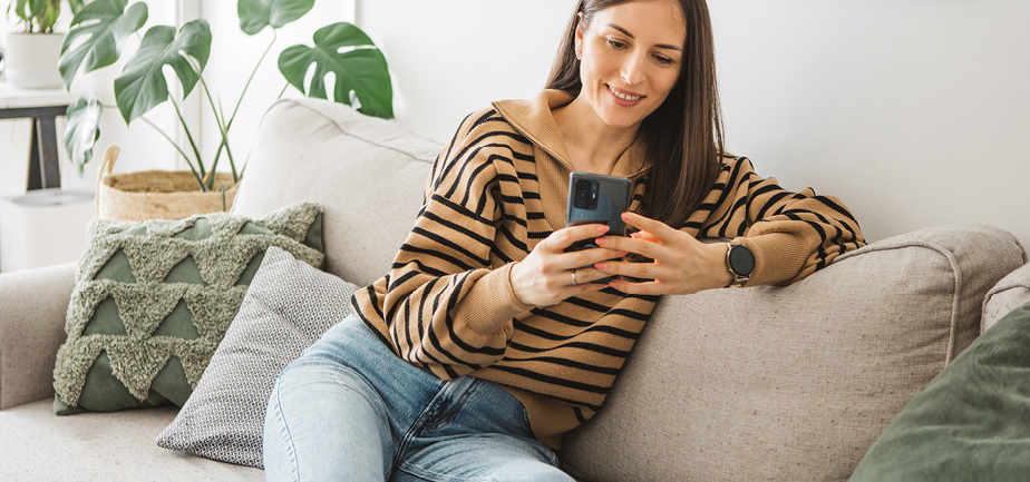 Smiling young woman using her mobile phone while sitting on sofa at home.