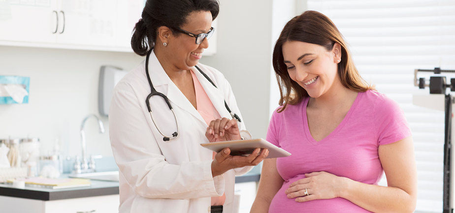 Doctor showing ultrasound scans to pregnant woman, using digital tablet
