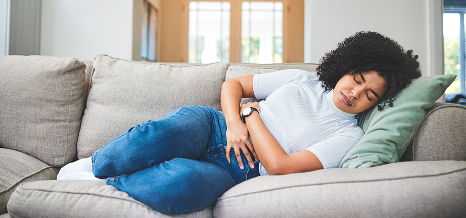Young woman holding her stomach in discomfort on the couch at home
