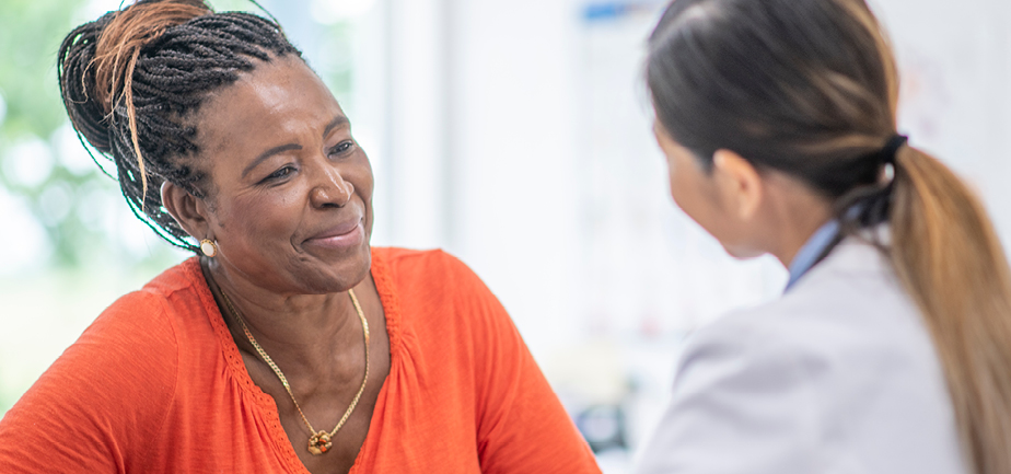A senior African American woman sits across the desk from her female doctor.