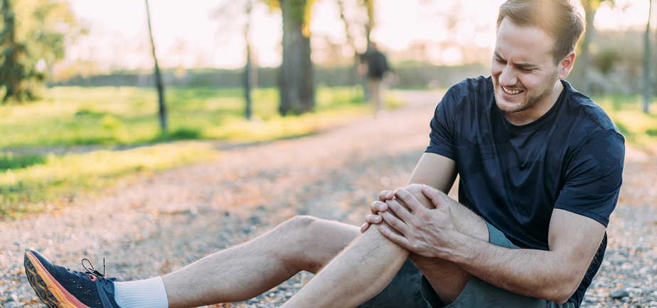 Sportsman holding his injured leg after jogging in the city park.