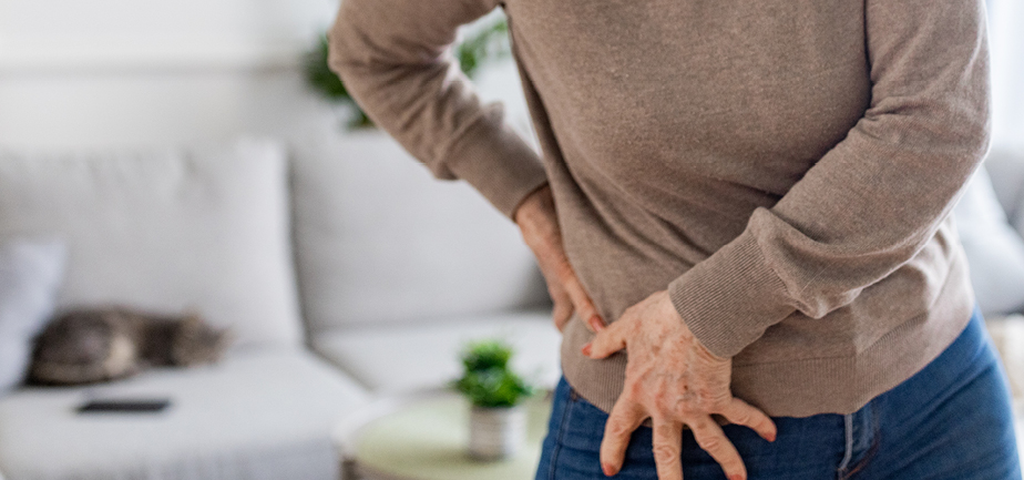 Senior woman having problems with hip pain while standing in living room at home.