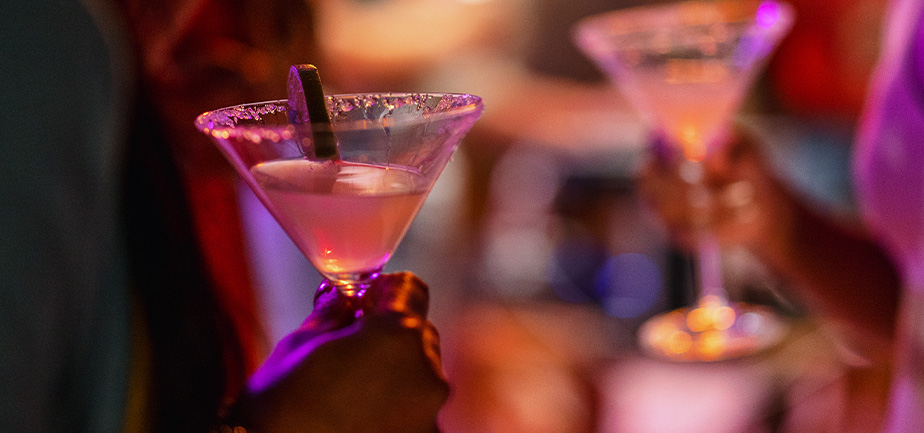 Close-up of a martini glass held by a female at a bar with purple lighting.