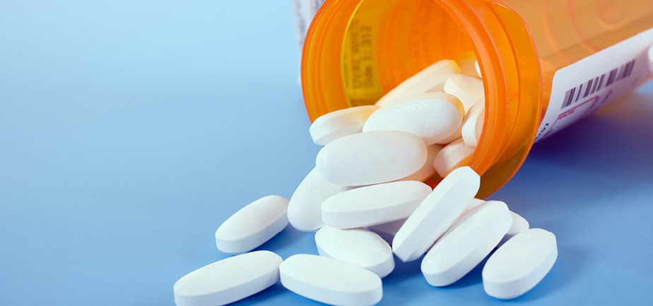Pills spilling out from medicine bottle on blue background 
