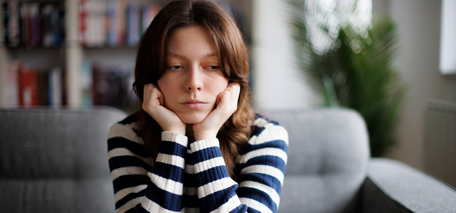 Sad unhappy teenage girl sitting on sofa at home