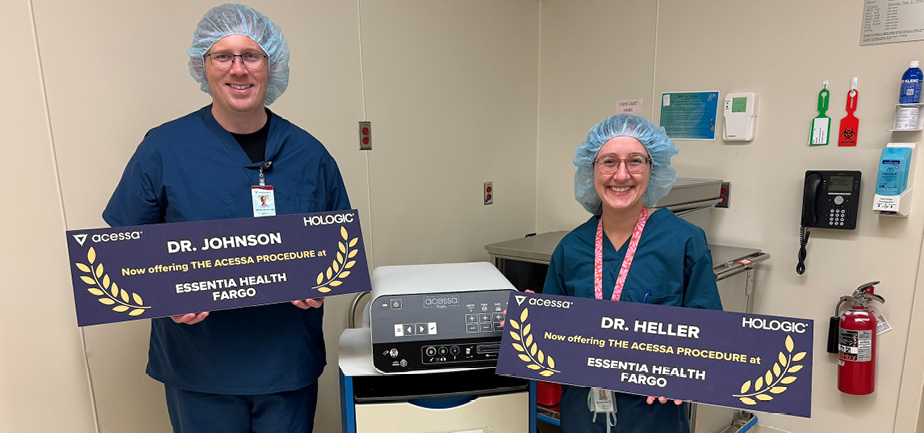 man and woman in scrubs holding signs with their names and by a medical device