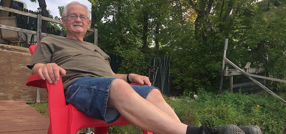 older man sitting in a red chair with his dog nearby