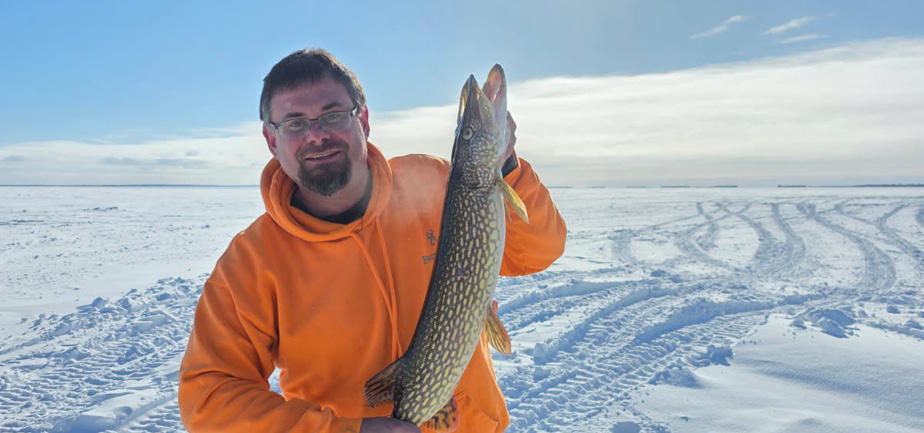man in an orange sweater standing outside holding a fish