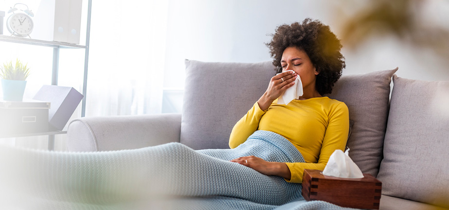 young woman sitting on couch blowing her nose