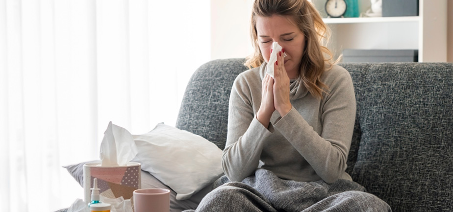 woman sick and blowing nose into a tissue on a couch