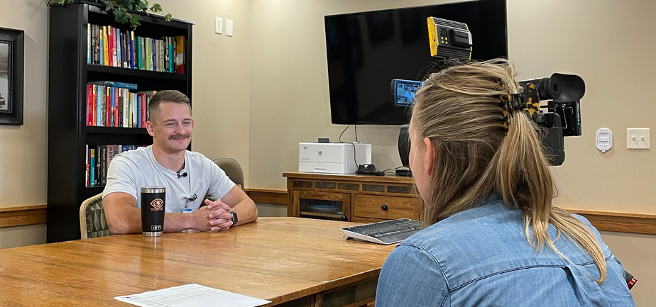 man speaking with female reporter sitting at a table