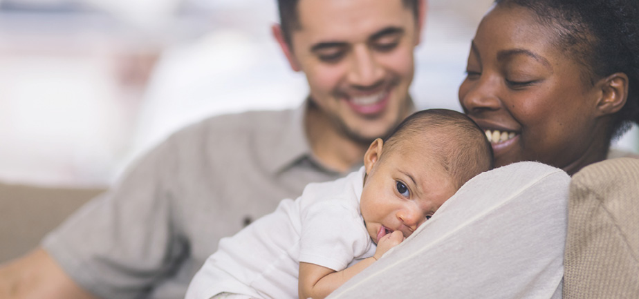 African American mother holds young baby to chest with father in background