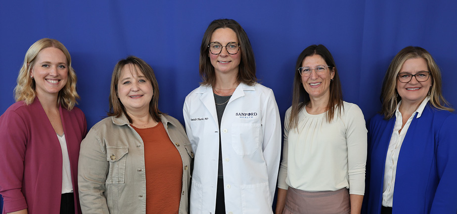 group of five women standing and smiling in front of a blue background