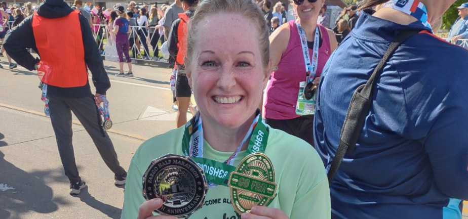 woman smiling and holding two running medals