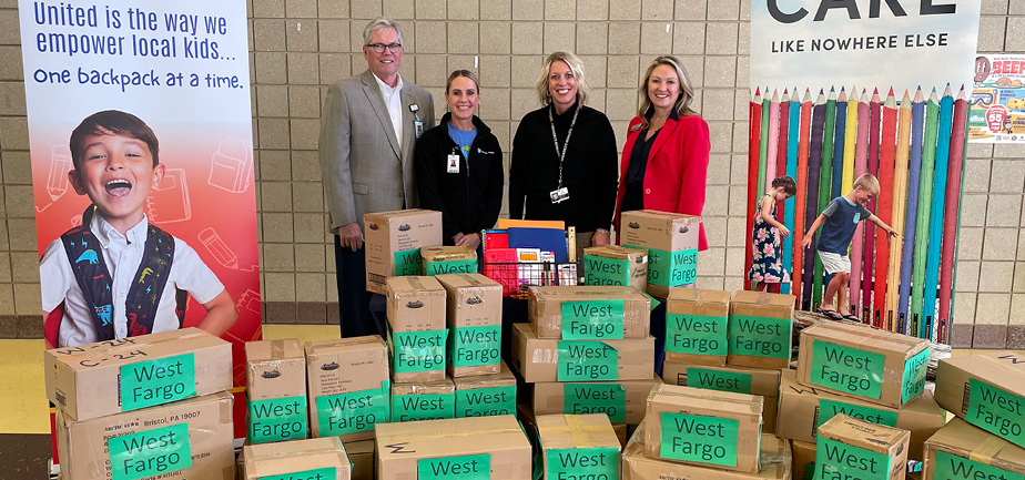 one man and three women standing in a group in front of several boxes of school supplies