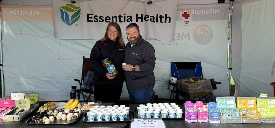 Man and woman smiling, under a tent and holding snacks in their hands for a bike race