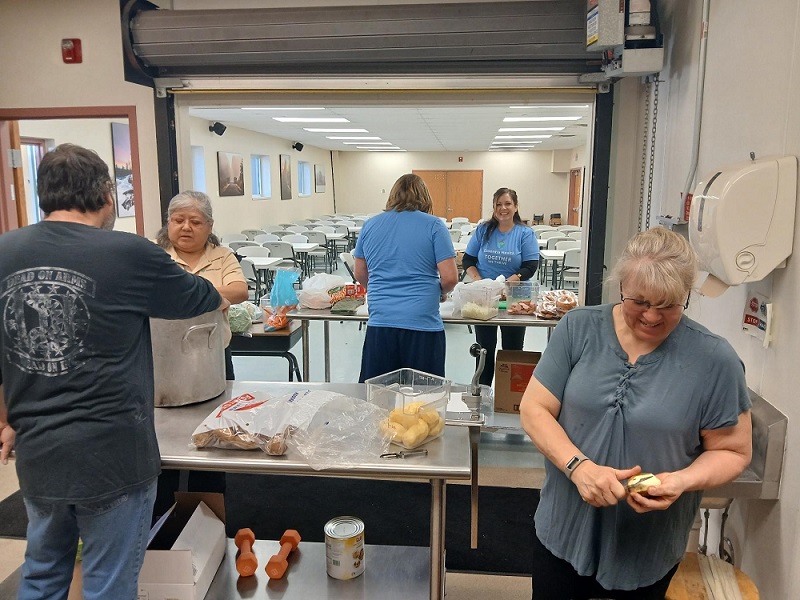 Four women and a man working together in a kitchen, preparing ingredients and cooking food.