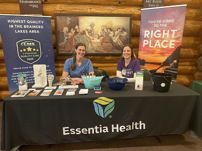 Two women smiling behind a table displaying books and an Essentia banner.