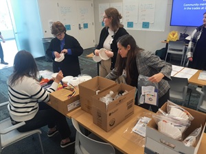 Four women surround tables with boxed items on the table