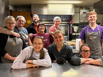 A kitchen crew wearing aprons smiles warmly while standing together