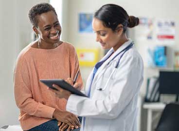 A female doctor with clip board talking to a smiling female patient